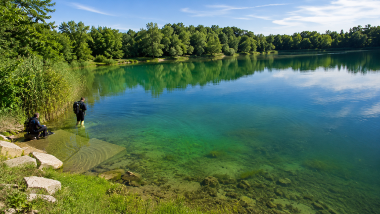 Widok na Kamionkę Piast w Opolu z przejrzystą, zielono-turkusową wodą, otoczoną drzewami, z nurkami przygotowującymi się do wejścia do akwenu.