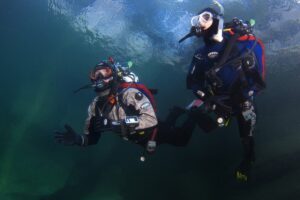 Dwóch nurków w suchych skafandrach podczas nurkowania pod wodą w trakcie kursu Dry Suit Diver